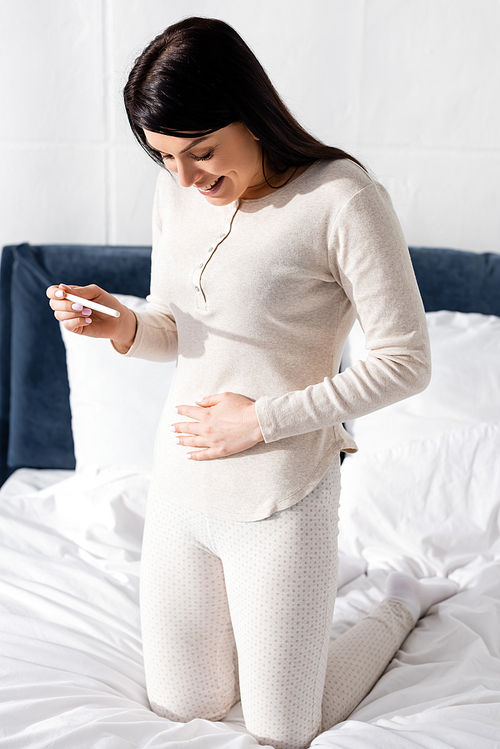 happy woman holding pregnancy test in bedroom