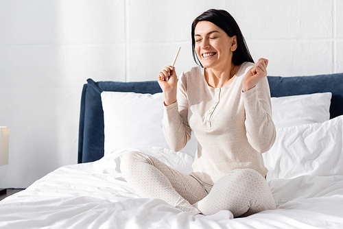 happy pregnant woman holding pregnancy test in bedroom