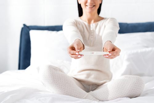 selective focus of cheerful woman holding pregnancy test in bedroom