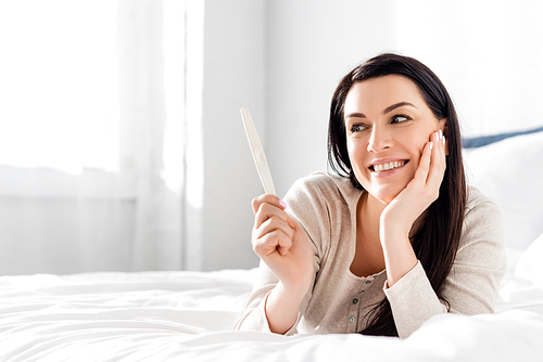 pregnant woman smiling and holding pregnancy test while lying on bed