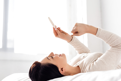cheerful woman smiling and looking at pregnancy test while lying on bed