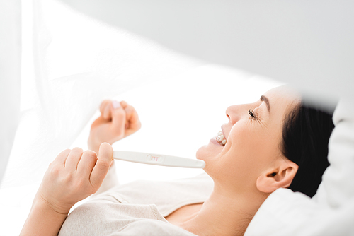 side view of positive woman looking at pregnancy test while lying on bed