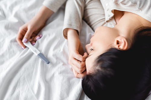 top view of depressed woman lying on bed near pregnancy test