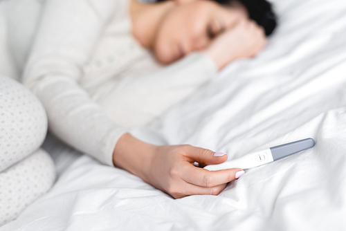 selective focus of depressed woman lying on bed and holding pregnancy test with negative result