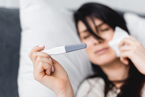 selective focus of sad woman looking at pregnancy test with negative result while lying on bed