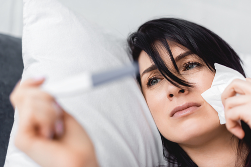 selective focus of upset woman looking at pregnancy test with negative result while lying on bed