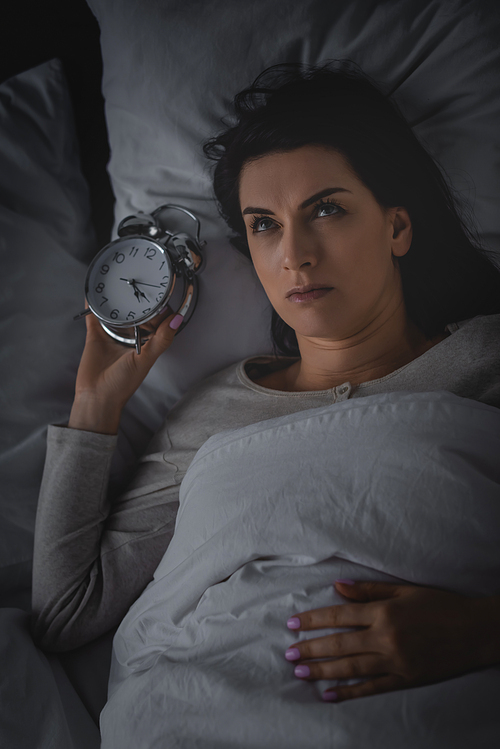 top view of awake woman lying on bed with alarm clock