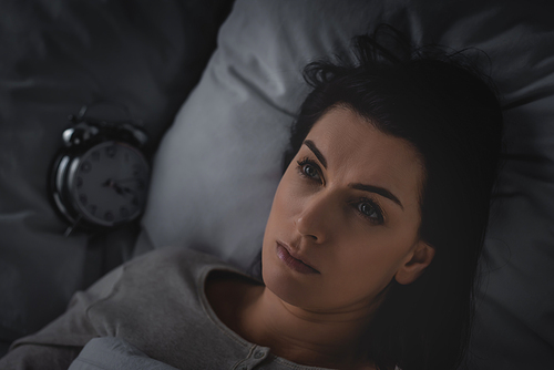 top view of awake woman with insomnia lying on bed near alarm clock