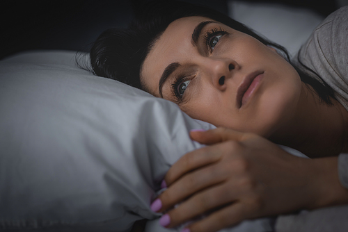 selective focus of displeased woman having insomnia while lying on bed at night
