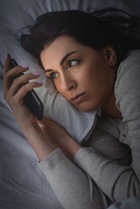 awake woman with insomnia using smartphone in bedroom