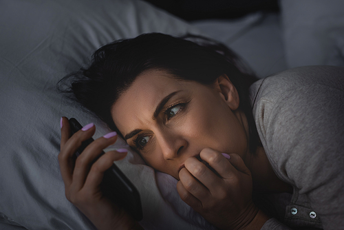 scared woman with insomnia using smartphone in bedroom