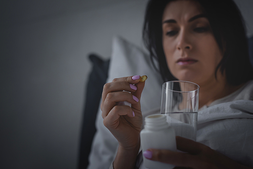 selective focus of woman with sleep disorder holding glass of water and sleeping pill in bedroom