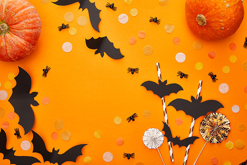 top view of pumpkin, bats and spiders with confetti on orange background, Halloween decoration