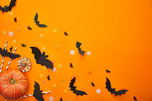 top view of pumpkin, bats and spiders with confetti on orange background, Halloween decoration