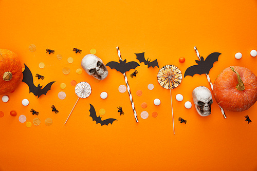 top view of pumpkin, skulls, bats and spiders with confetti on orange background, Halloween decoration