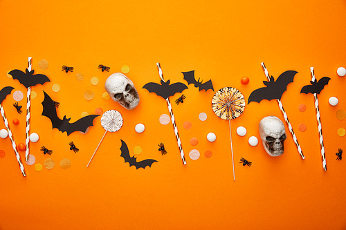 top view of skulls, bats and spiders with confetti on orange background, Halloween decoration