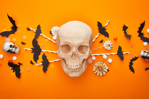 top view of skull with bats and spiders and confetti on orange background, Halloween decoration