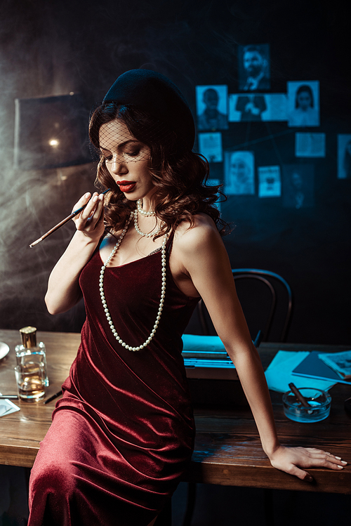 Woman in dress sitting on table and holding mouthpiece in dark office