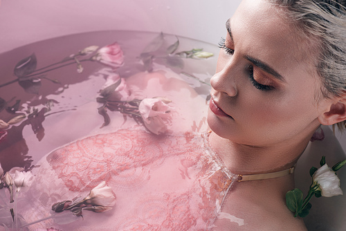 beautiful woman lying in clear water with flowers in white bathtub, pink toned image