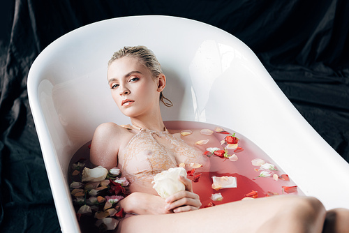 beautiful wet and sexy blonde woman lying in bathtub with pink water and petals