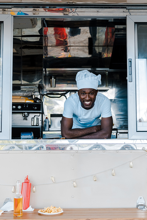 happy african american man in chef uniform smiling from food truck