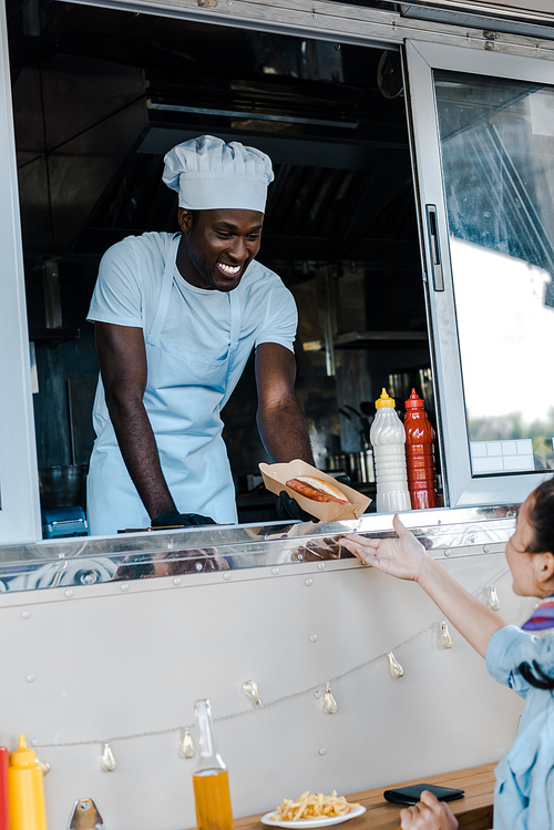 selective focus of cheerful african american man giving carton plate with french fries to customer
