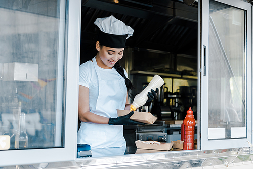 cheerful asian woman holding carton plate and mayonnaise bottle in food truck