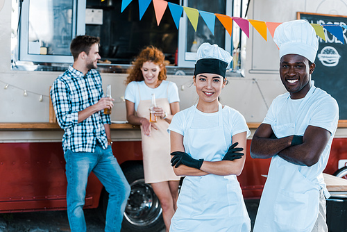 selective focus of cheerful multicultural chefs smiling near food truck and customers