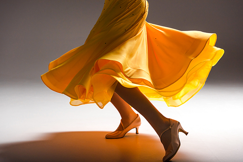 cropped view of elegant young ballroom dancer in yellow dress dancing in dark