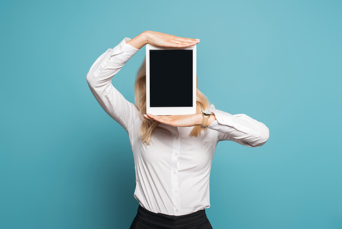 businesswoman in white blouse obscuring face with digital tablet with blank screen on blue background