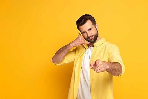 Handsome man showing call sign and pointing with finger at camera on yellow background
