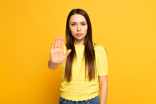 Attractive girl showing stop gesture while  on yellow background