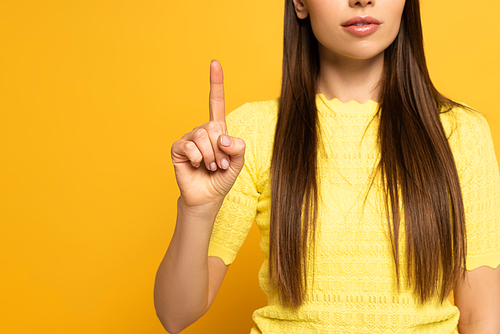 Cropped view of young woman pointing with finger on yellow background