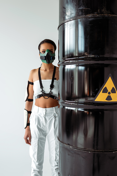 futuristic african american woman in safety mask near radioactive waste barrels isolated on white