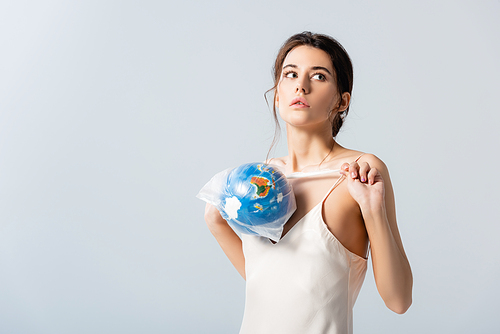 young woman holding plastic bag with globe and looking away isolated on white, ecology concept