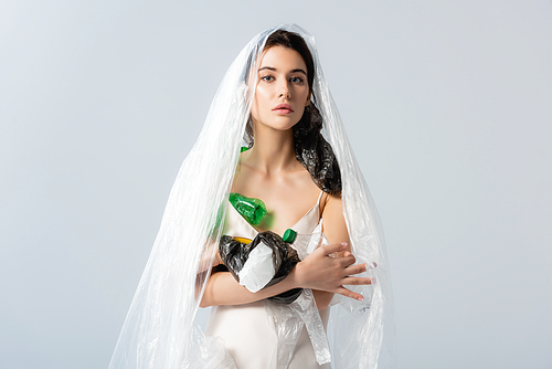 young woman with plastic bag on head holding empty bottles and  isolated on grey, ecology concept