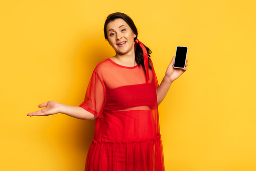 pregnant woman in red outfit holding smartphone with blank screen while standingon yellow