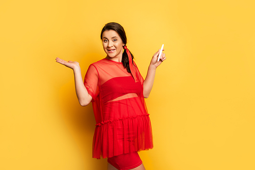 pregnant woman in red outfit holding pregnancy test while standing on yellow