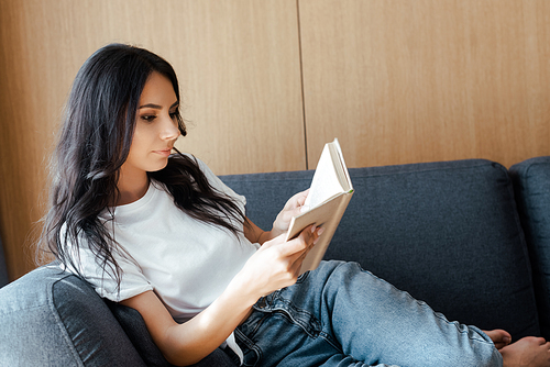 beautiful young woman reading book on sofa at home