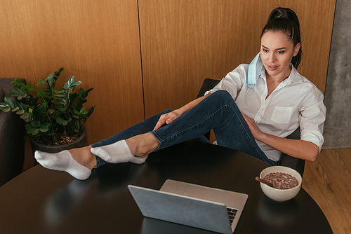 high angle view of young woman looking at laptop near bowl with breakfast on table