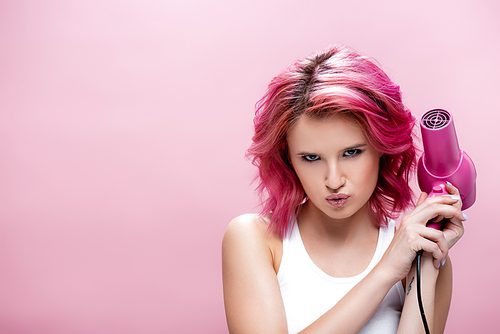 serious young woman with colorful hair holding hairdryer isolated on pink