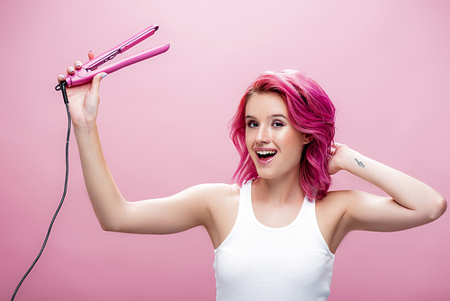 young woman with colorful hair holding straightener isolated on pink