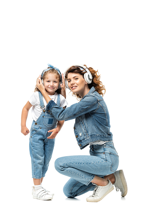 mother and daughter in denim outfits listening music in headphones isolated on white
