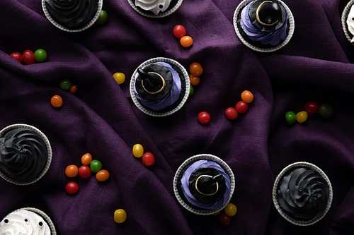 top view of delicious Halloween cupcakes with bonbons on purple cloth
