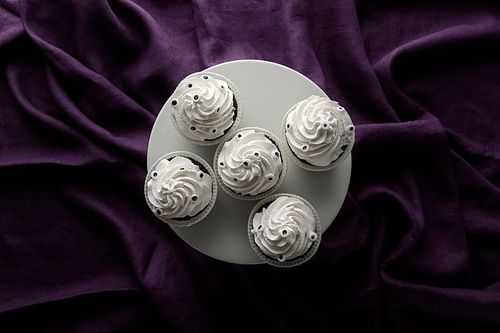 top view of delicious Halloween cupcakes with white cream on stand on purple cloth