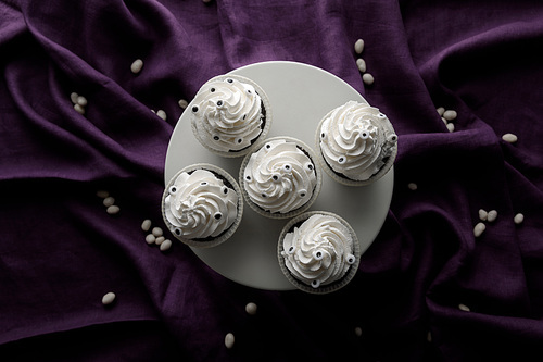 top view of delicious Halloween cupcakes with white cream on stand on purple cloth