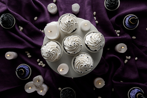 top view of delicious Halloween cupcakes near burning candles on purple cloth
