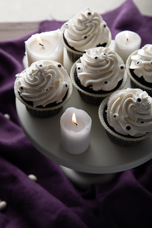 delicious Halloween cupcakes on stand near burning candles on purple cloth