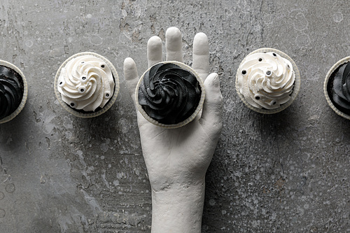 top view of delicious Halloween cupcake in decorative hand on concrete grey surface