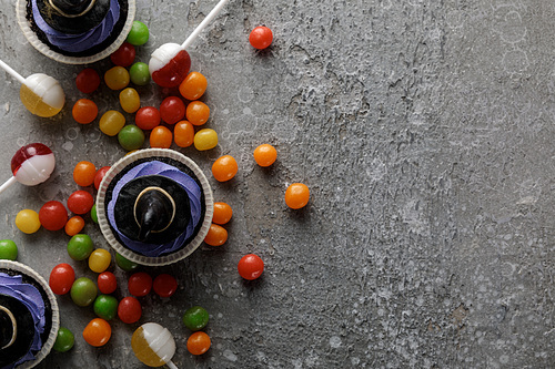 top view of delicious Halloween cupcakes, lollipops and bonbons on concrete grey surface